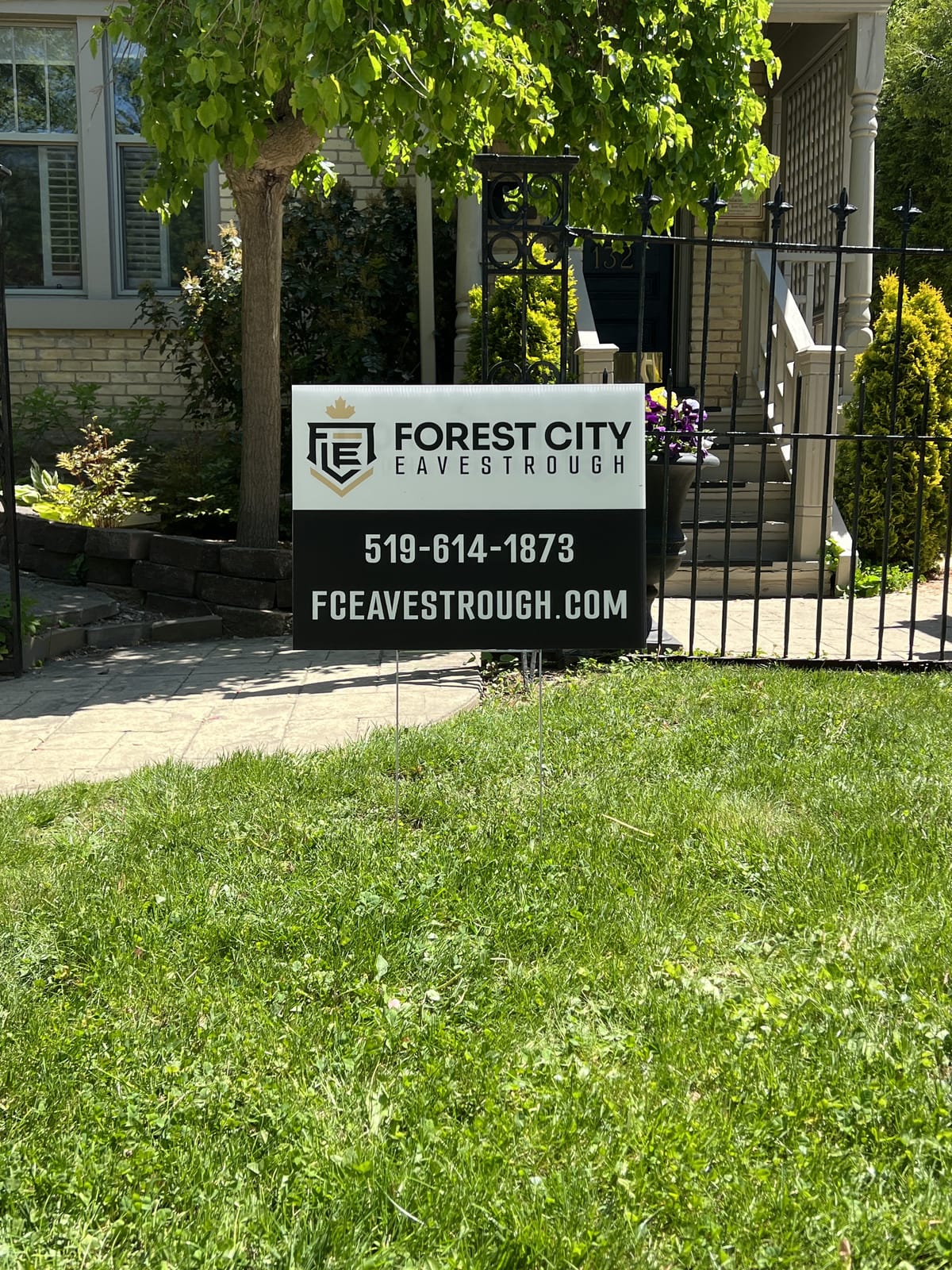 FCE yard sign on a green lawn in front of a brick home with a black iron fence in the London, Ontario area
