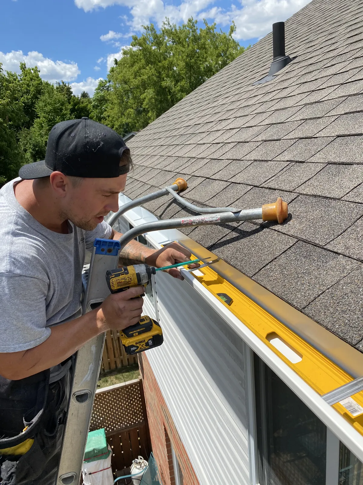 Installer on a ladder drilling seamless eavestrough into place at the roofline of a home in the London, Ontario area