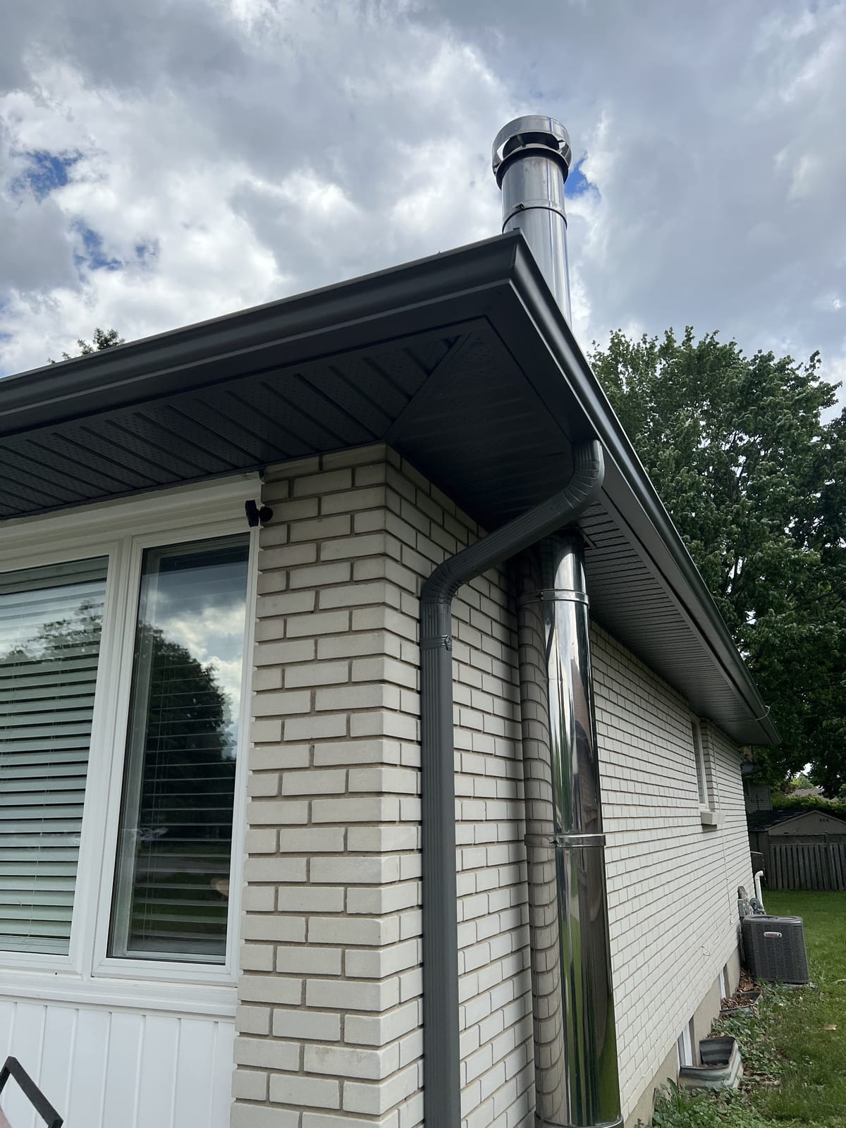 Grey seamless eavestrough, downspout, soffit and fascia on a light brick home with a chimney flue, London, Ontario area