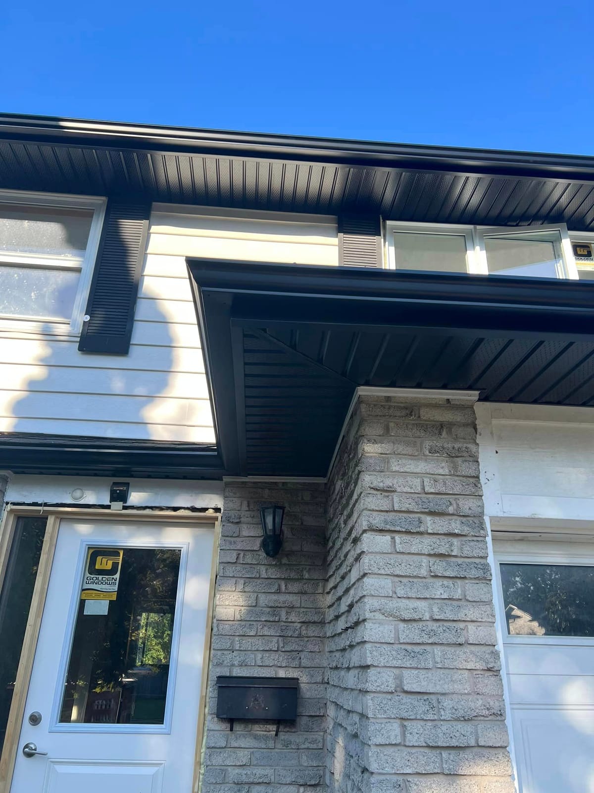 Black seamless eavestrough, soffit and fascia above a white front door on a stone and white-sided home, London, Ontario area