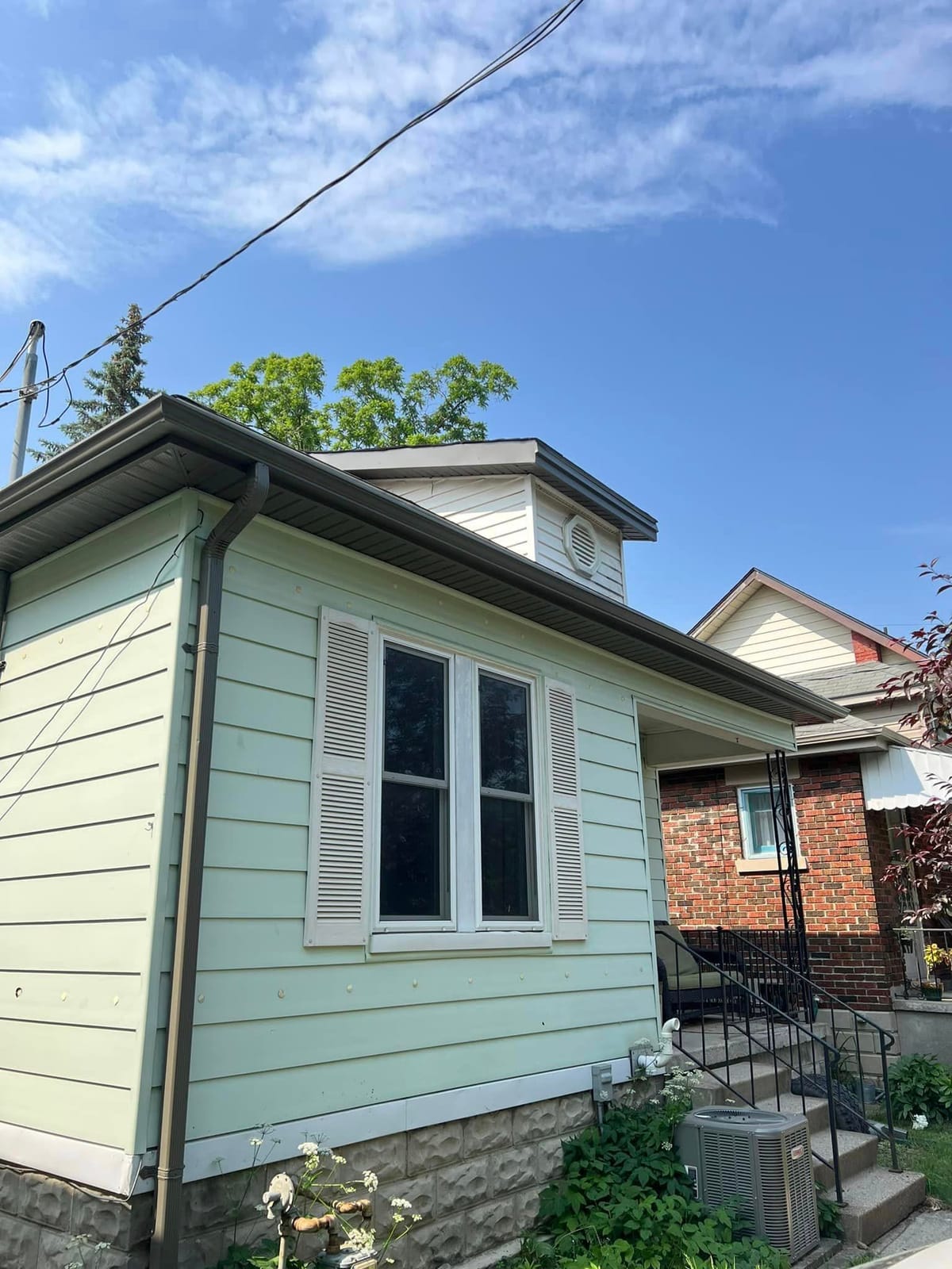 Brown seamless eavestrough, downspout, soffit and fascia on a mint green home with white shutters in the London, Ontario area