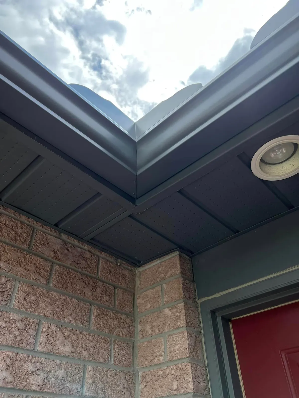 Close view of a grey seamless eavestrough corner with soffit and fascia above a red door, London, Ontario area