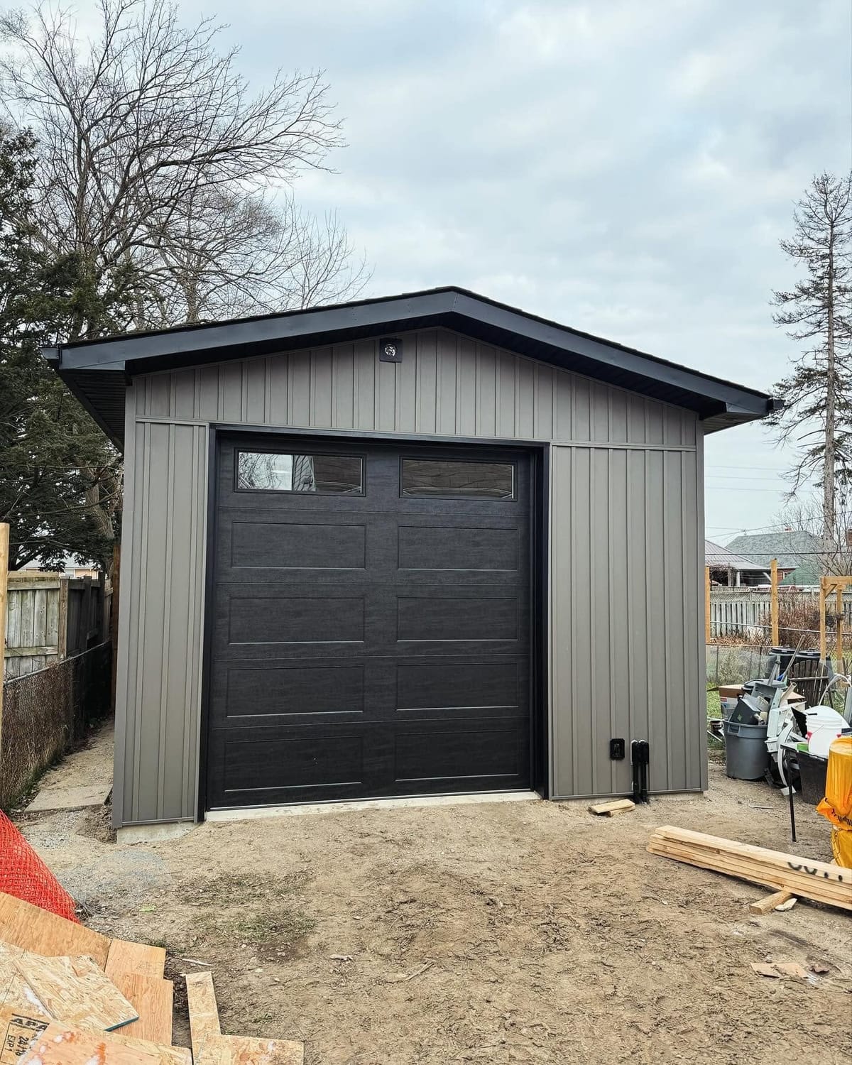 Grey vertical vinyl siding with black soffit, fascia and a black overhead door on a detached garage, London, Ontario area