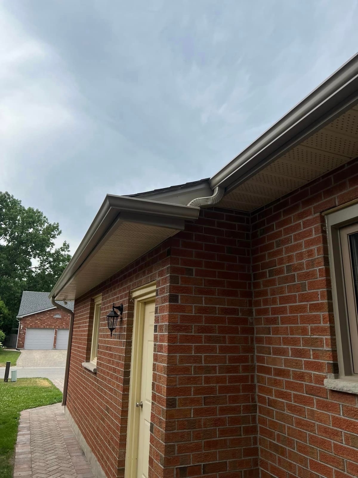 Tan seamless eavestrough, soffit and fascia on a red brick home with a cream door in the London, Ontario area