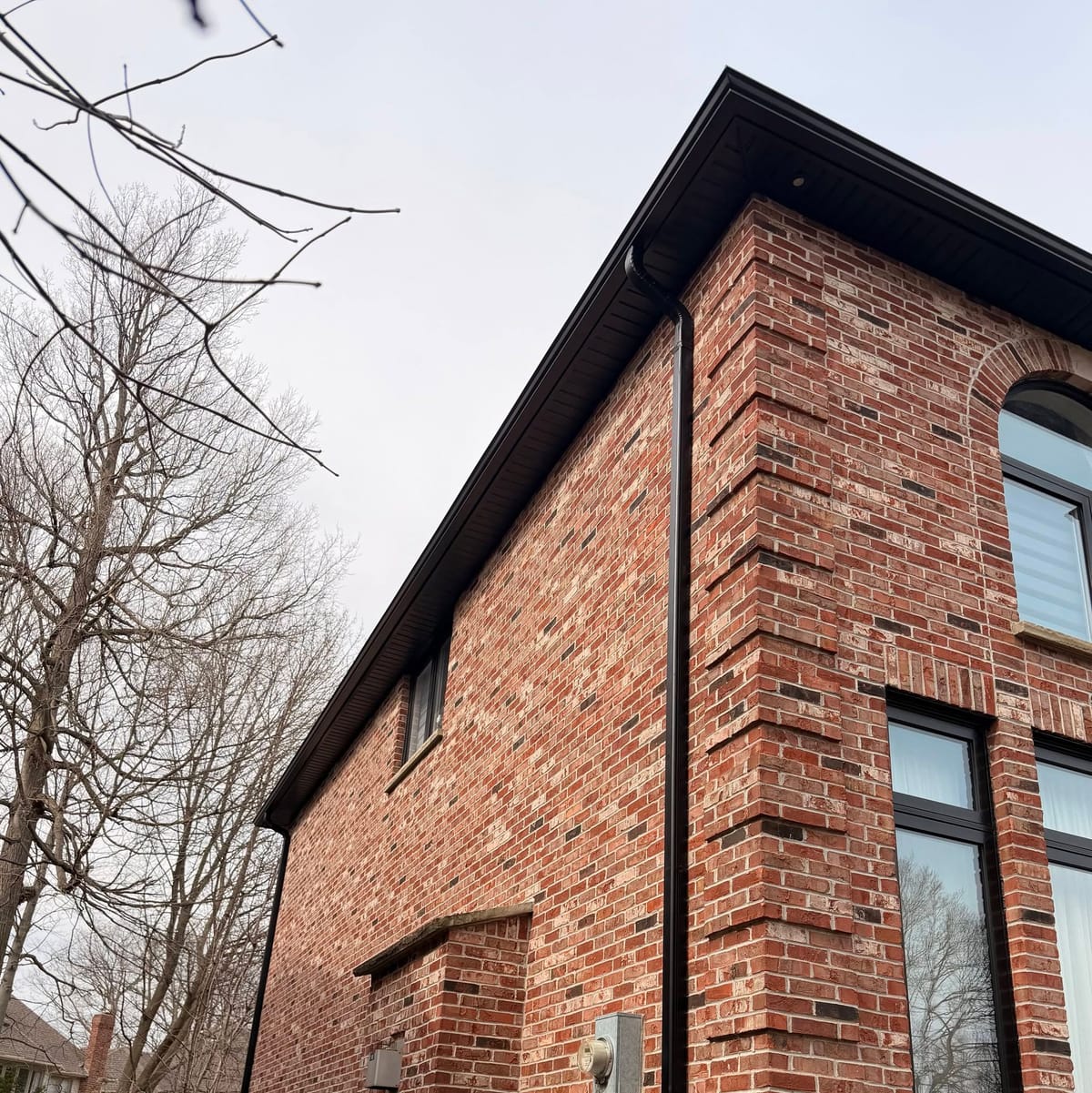 Black soffit, fascia and seamless eavestrough along the roof edge of a red brick home in the London, Ontario area, seen from below