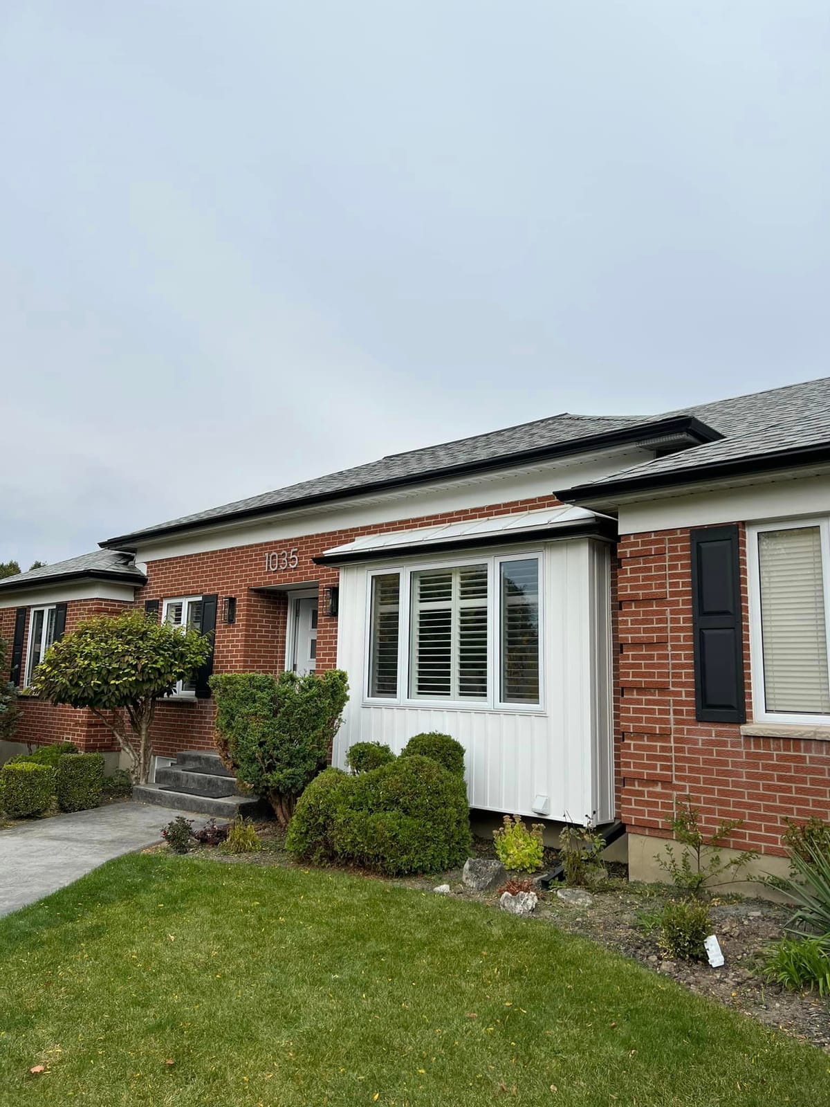 Black seamless eavestrough on a red brick bungalow with a white bay window and black shutters in the London, Ontario area
