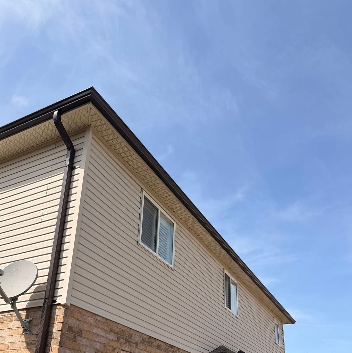 Brown seamless eavestrough and downspout on a two-storey home with tan siding and a brick base in the London, Ontario area