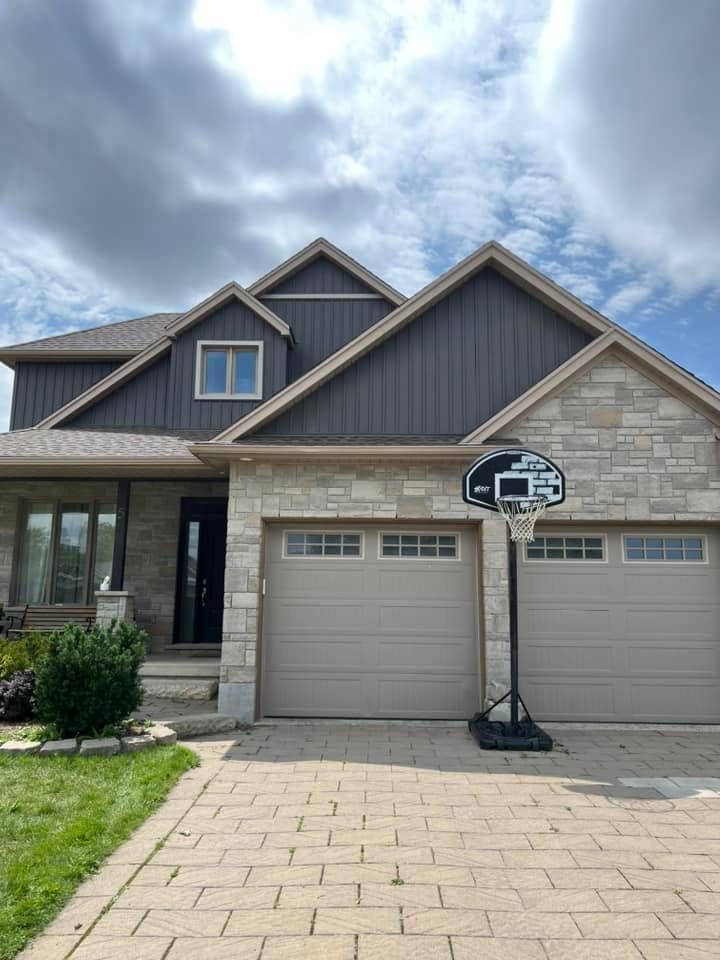 Grey vertical vinyl siding with soffit, fascia and seamless eavestrough above a stone double garage, London, Ontario area