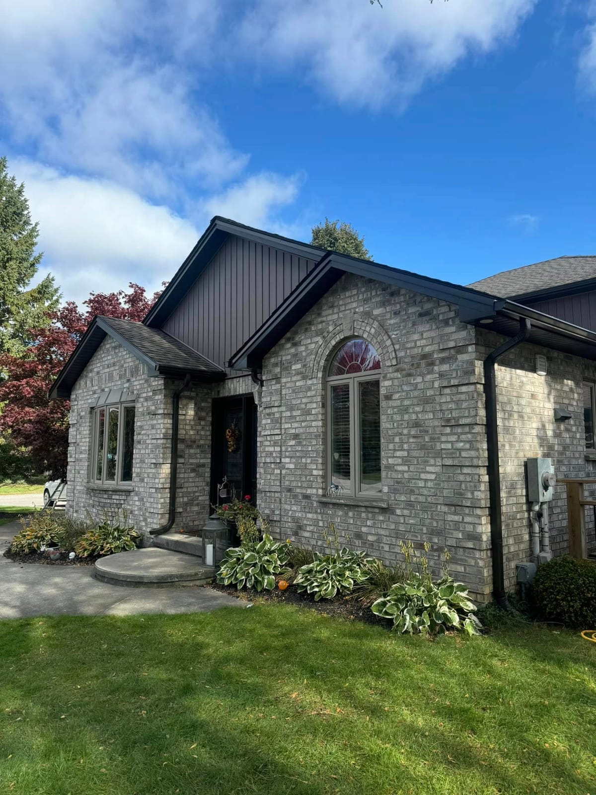 Dark vinyl siding, black downspout, soffit and fascia on a grey brick bungalow with an arched window, London, Ontario area