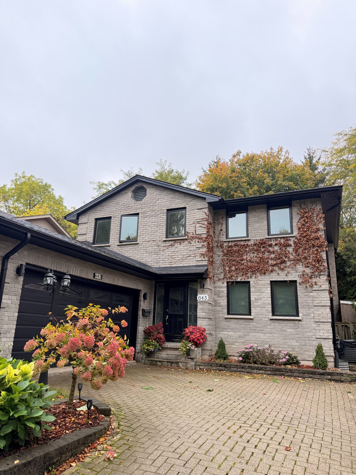 Black seamless eavestrough, downspout, soffit and fascia on a two-storey light brick home with a black garage door, London, Ontario area