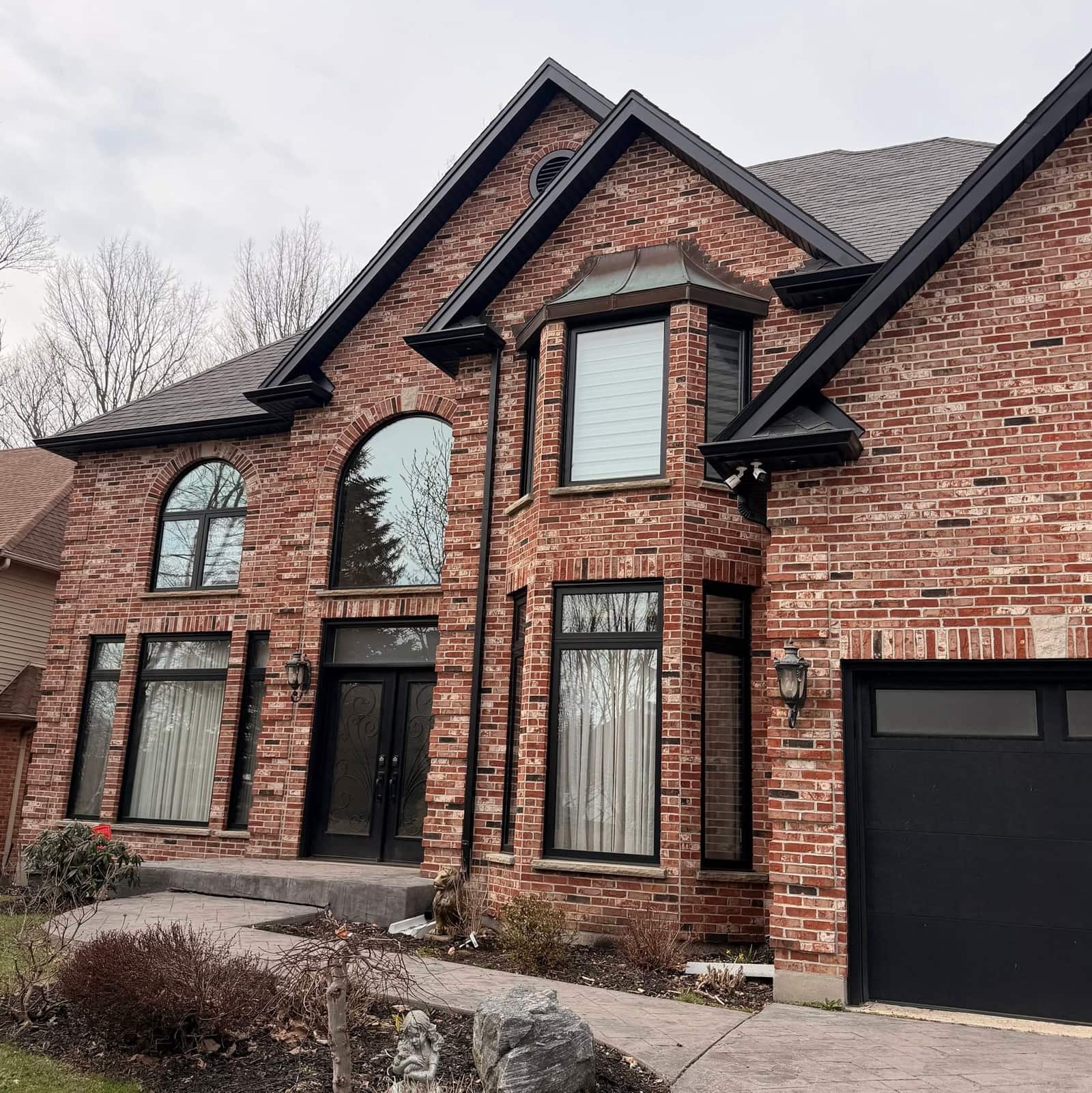 A two-storey red brick house with black seamless eavestrough, soffit and fascia along its gables.