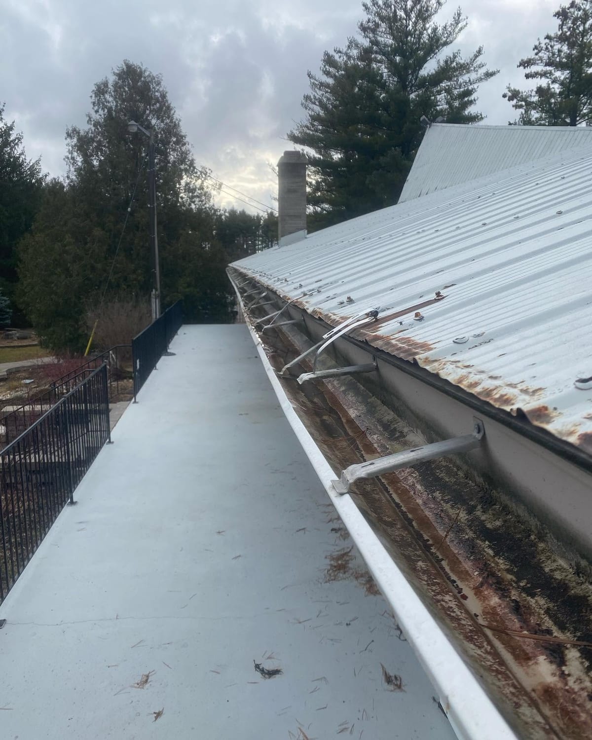 Old white eavestrough along a metal roof edge, rusted and stained inside, with bent and loose hangers