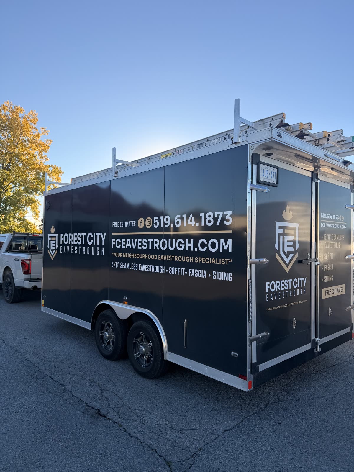 Forest City Eavestrough work trailer with ladders on the roof rack, parked in the London, Ontario area