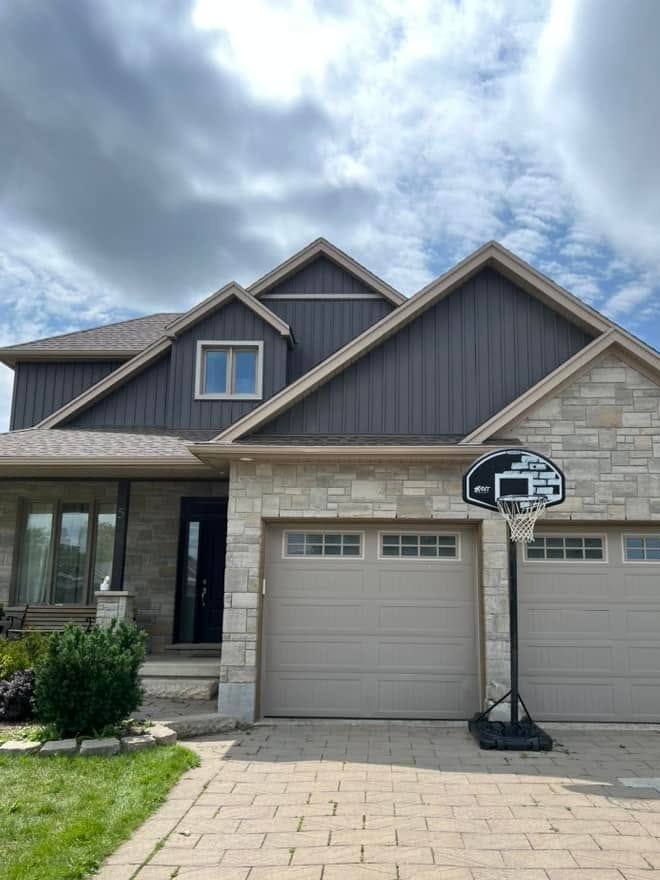 The same home after: dark grey vertical siding on the gables, with the stone front and garage unchanged.