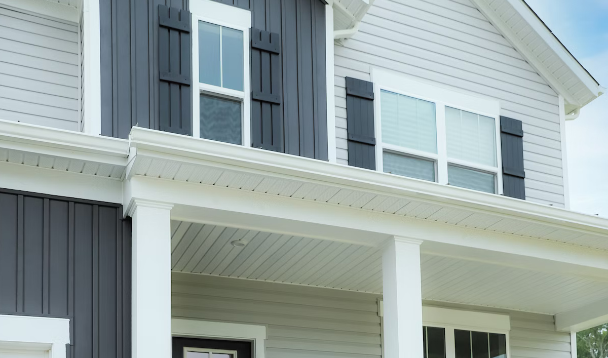 Grey vinyl siding and board and batten with white soffit, fascia and eavestrough over a front porch.